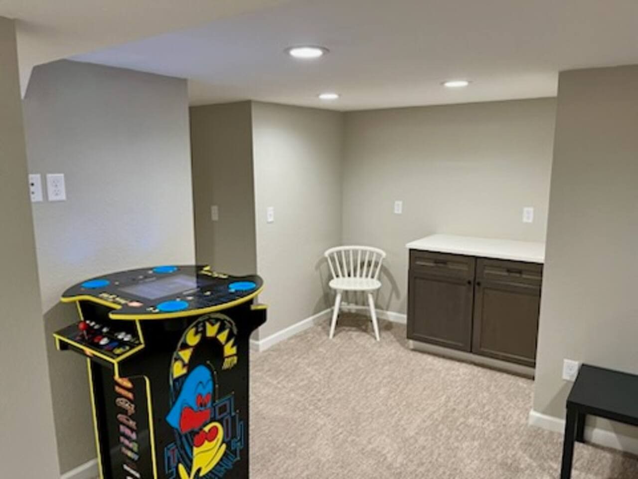 A room with a gaming machine, a white chair, and a cabinet.