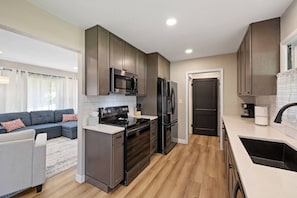 A modern kitchen with dark wood cabinets, stainless steel appliances, and a grey sofa in the adjacent living area. - Sleeps 10, Available Garage! (Sturgis)