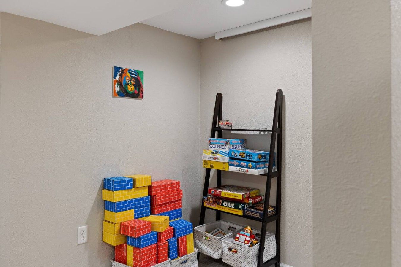 A room with a stack of colorful building blocks, a shelf with board games, and a small painting on the wall.