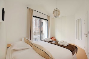 Une chambre d’hôtel avec un lit, une fenêtre avec des rideaux, un luminaire suspendu, une porte et un miroir.
