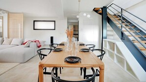 Un comedor moderno con una mesa de madera, sillas negras y una escalera con barandilla de metal.