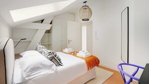 Un dormitorio moderno con tragaluz, una cama con ropa blanca, una lámpara colgante y una silla morada.