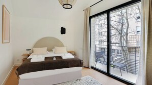 Un dormitorio con una cama grande, una mesita de noche, una lámpara, una ventana con cortinas y vistas al exterior.