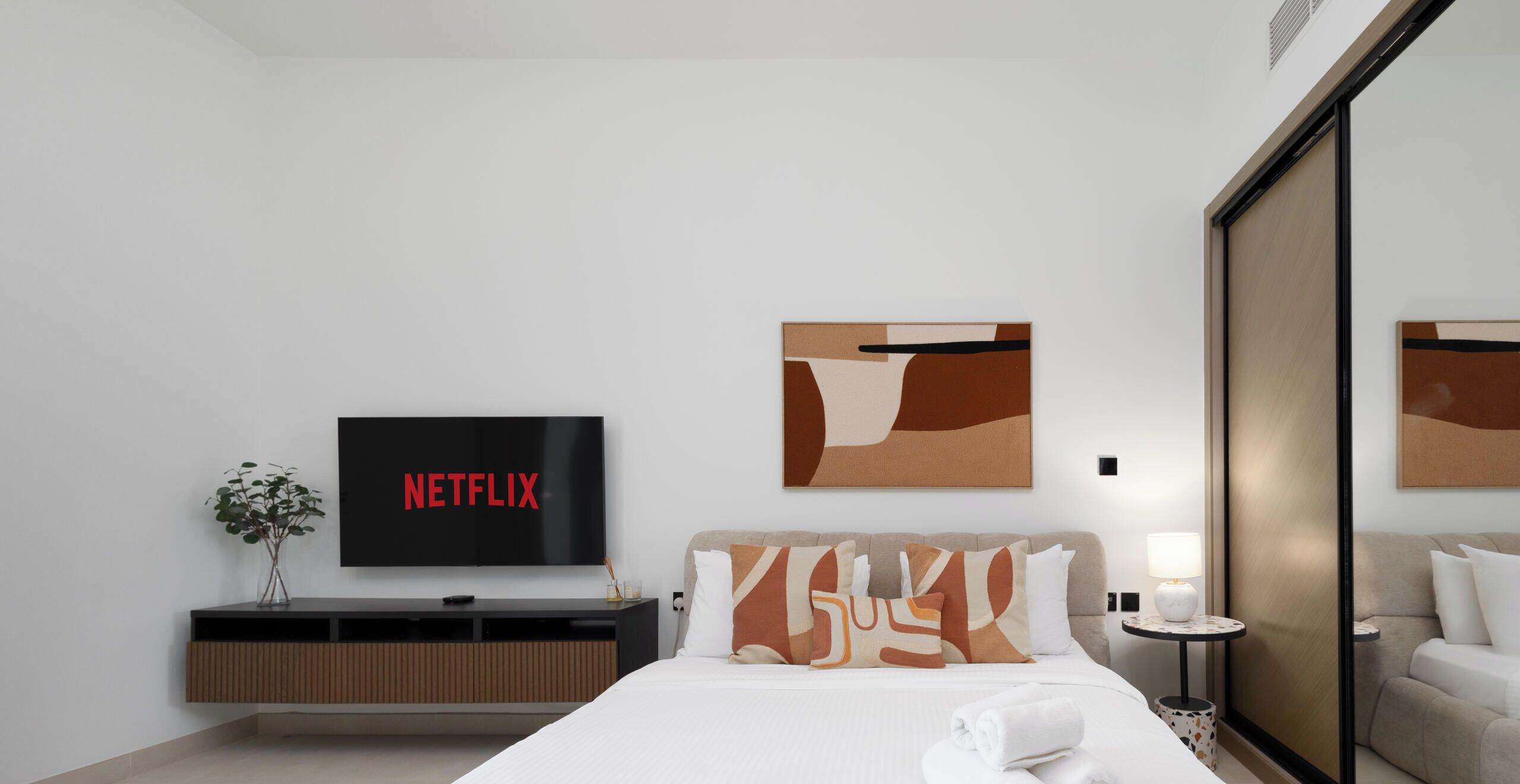 Een moderne hotelkamer met een flatscreen televisie, abstracte wanddecoratie, een nachtkastje met lamp en een bank.