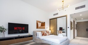 Ein modernes Hotelzimmer mit großem Flachbildfernseher, einer Couch, einem Bett und einem Spiegel.