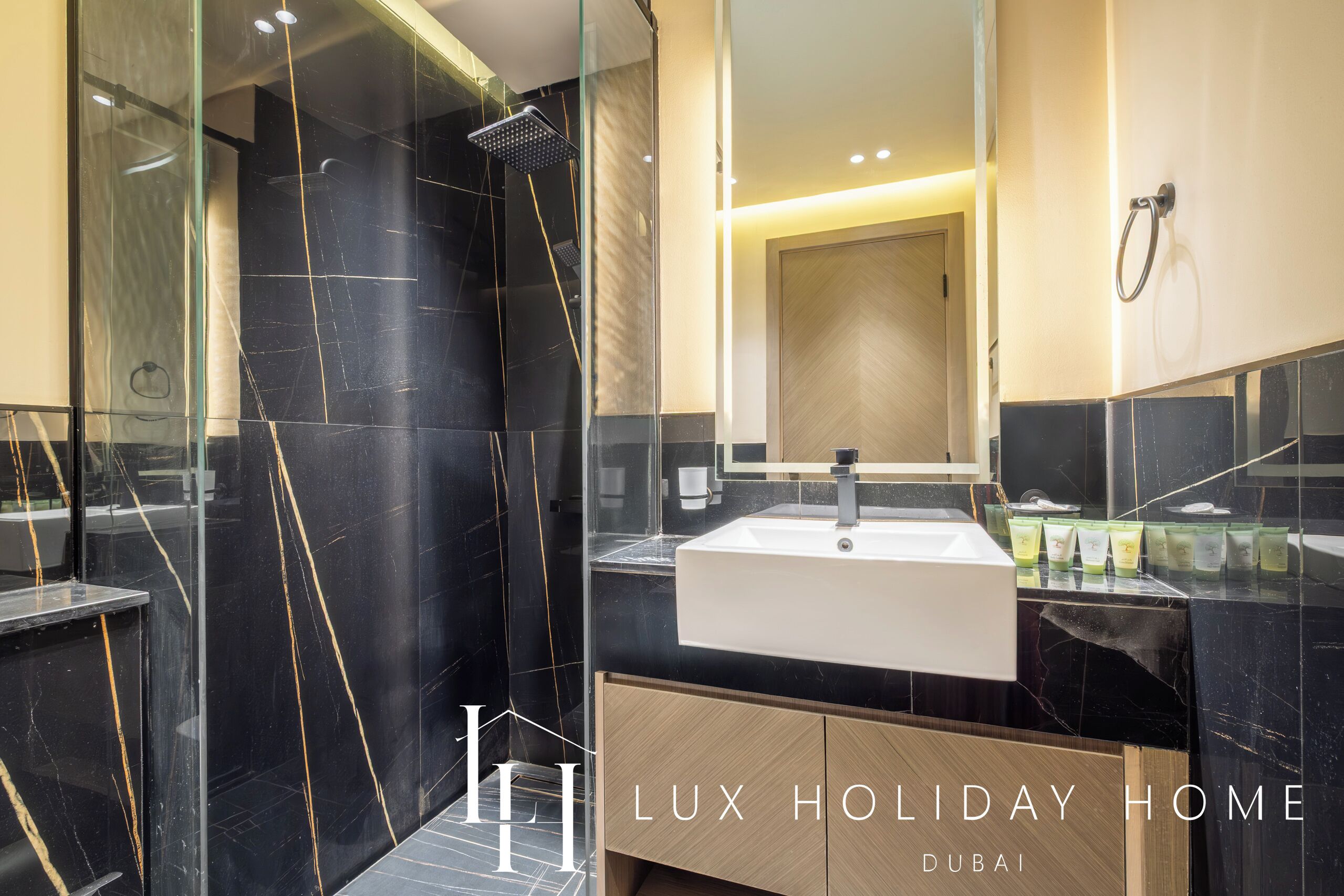 A modern bathroom with a glass-enclosed shower, a large mirror, and a vanity with a sink and toiletries.