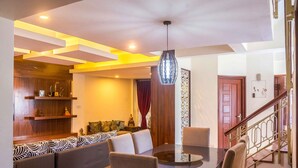A dining area with a round table, cushioned seating, and a hanging light fixture.