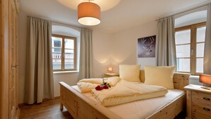 A wooden bed with a headboard, a bedside table with a lamp, and a window with curtains. - Jagerhaus Apartment Near ski Area (Hopfgarten im Brixental)