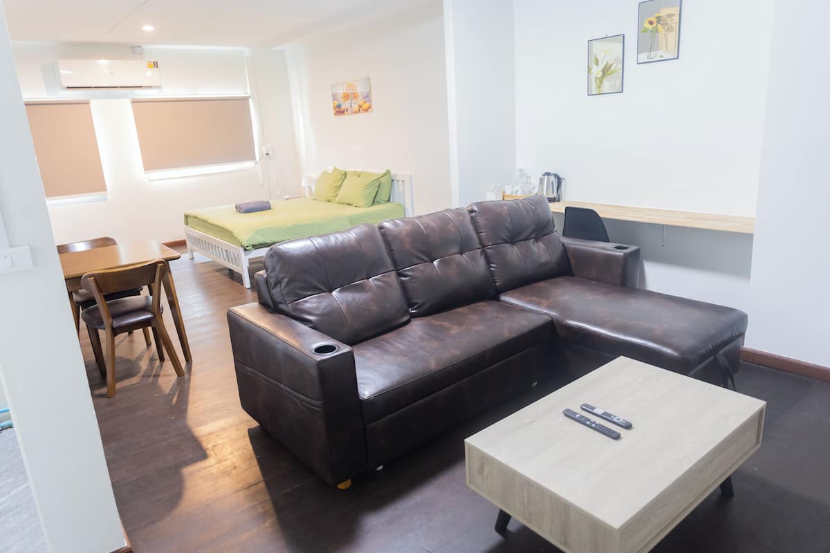 A modern living room with a leather sofa, a wooden coffee table, and a bed with green bedding.