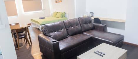 A modern living room with a leather sofa, a wooden coffee table, and a bed with green bedding.