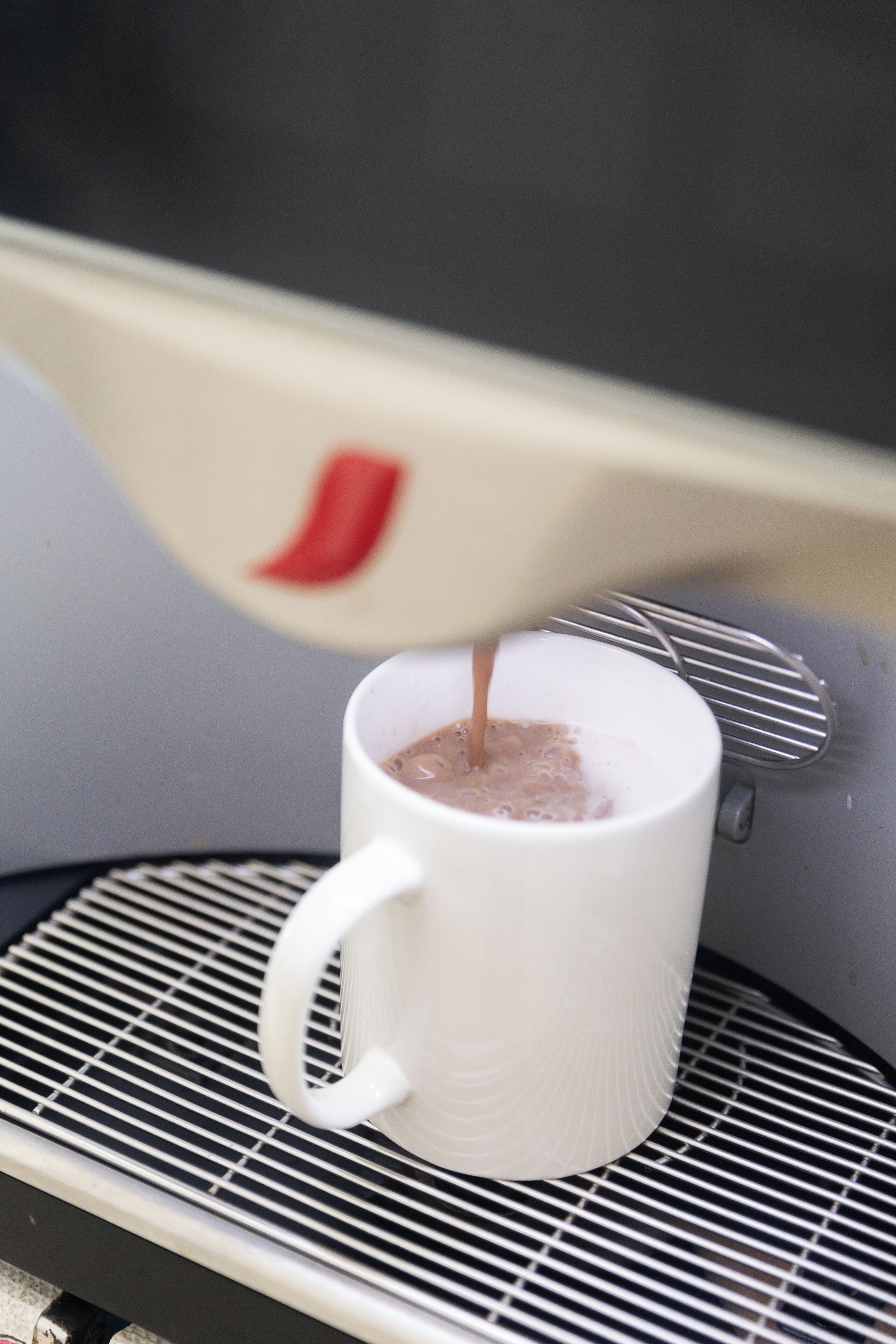 A white mug on a metal tray with a beverage being poured into it.