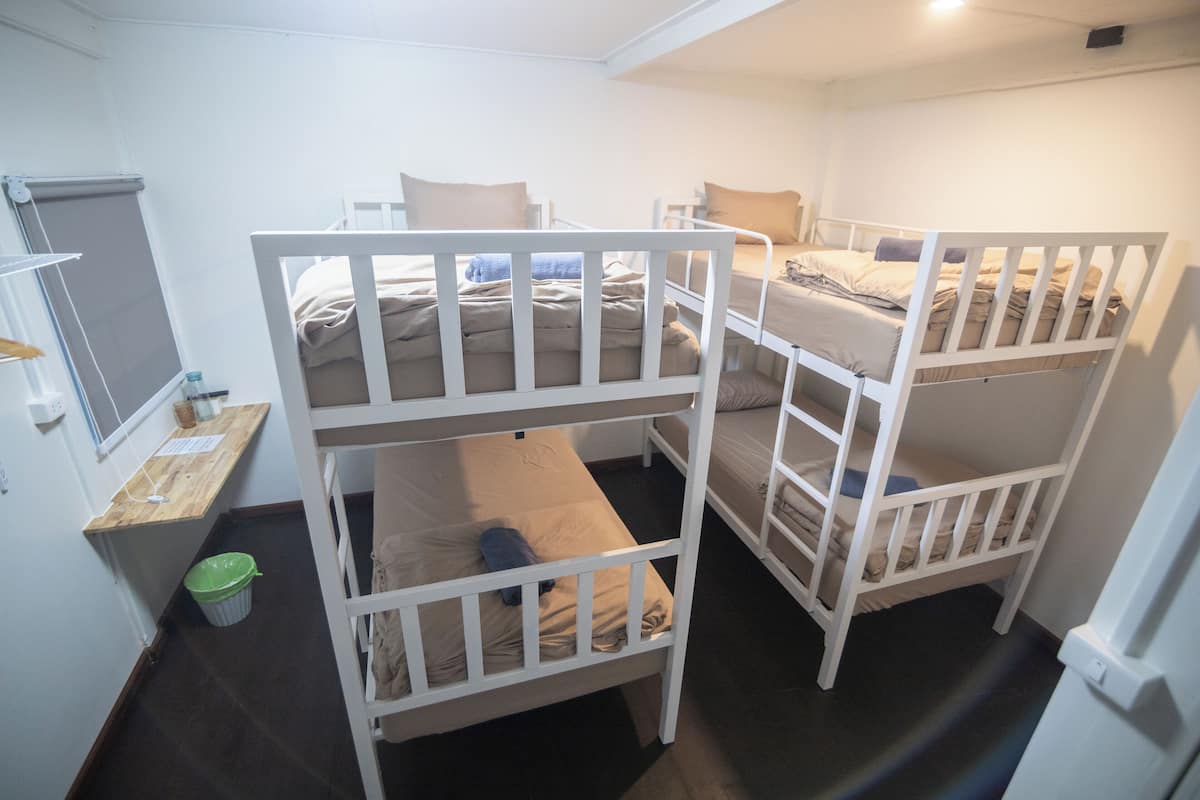 A bunk bed room with a desk and a trash bin.