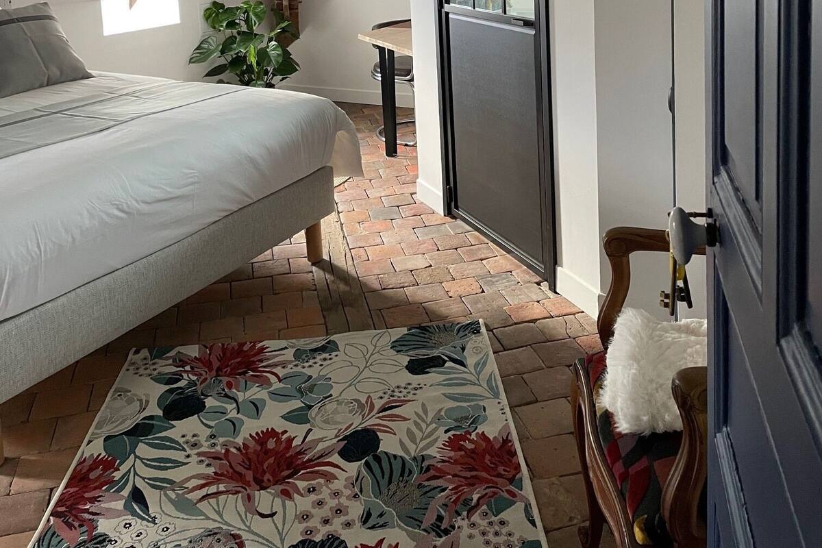 Une chambre à coucher avec un lit, une fenêtre, une porte, une plante et un tapis à motifs.