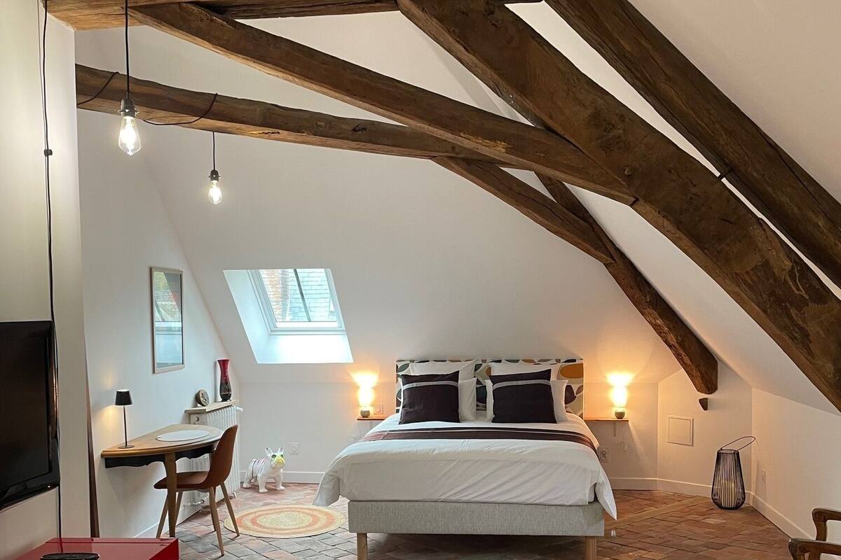 Une chambre aménagée dans les combles, avec des poutres apparentes, un lit, un bureau et une armoire rouge.