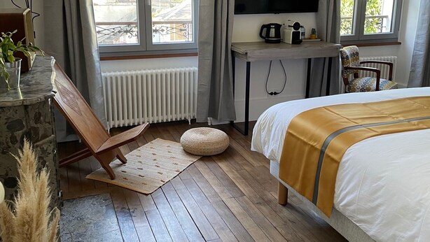 A bedroom with a bed, a TV, a desk with a kettle, and a window with curtains. - Le Petit Monde de Molly (Toucy)