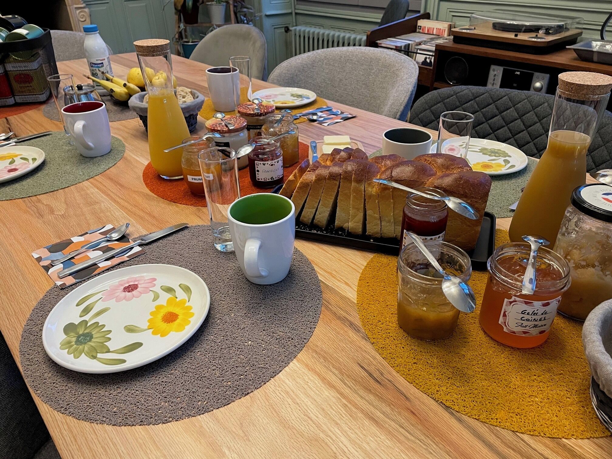 A breakfast table with a loaf of bread, a green mug, and various condiments.