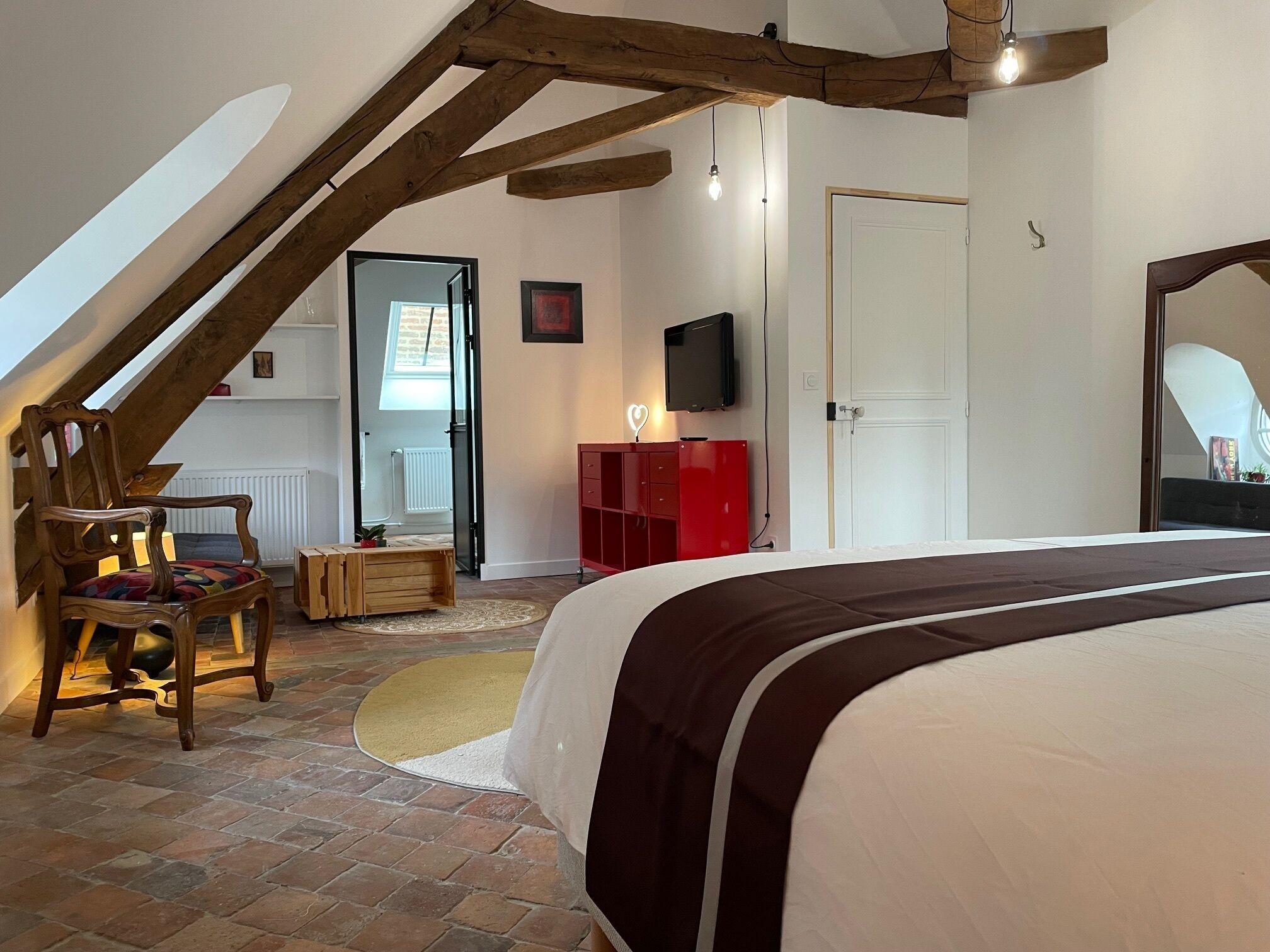 Un dormitorio con techo inclinado, una cama, un televisor, un armario rojo y una silla de madera.