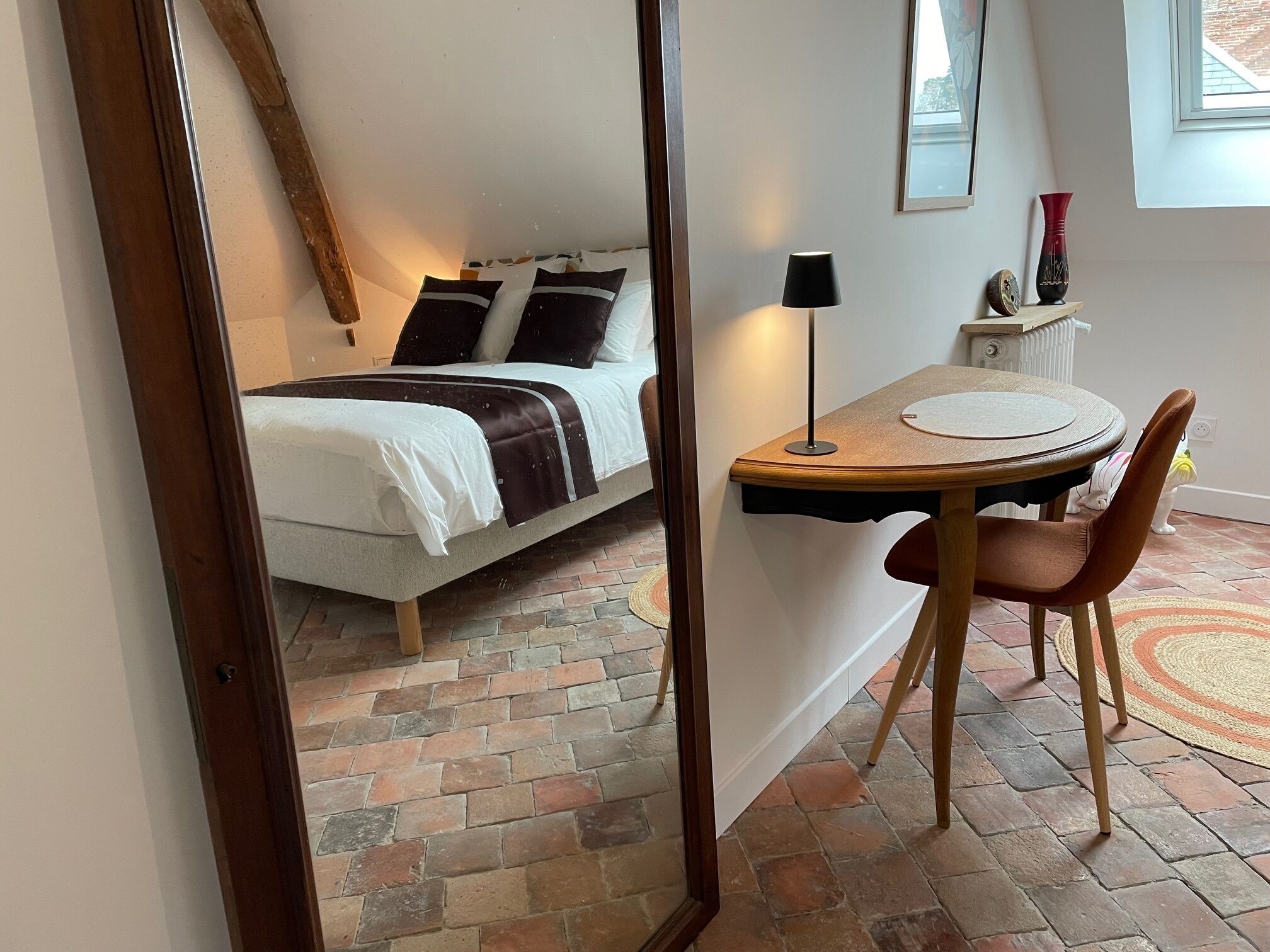 A bedroom with a bed, bedside table, lamp, and a small table with a chair.