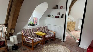 A loft-style room with a wooden ceiling, a sofa, a small table, a lamp, a patterned rug, and a window with a cityscape view. - Le Petit Monde de Molly (Toucy)