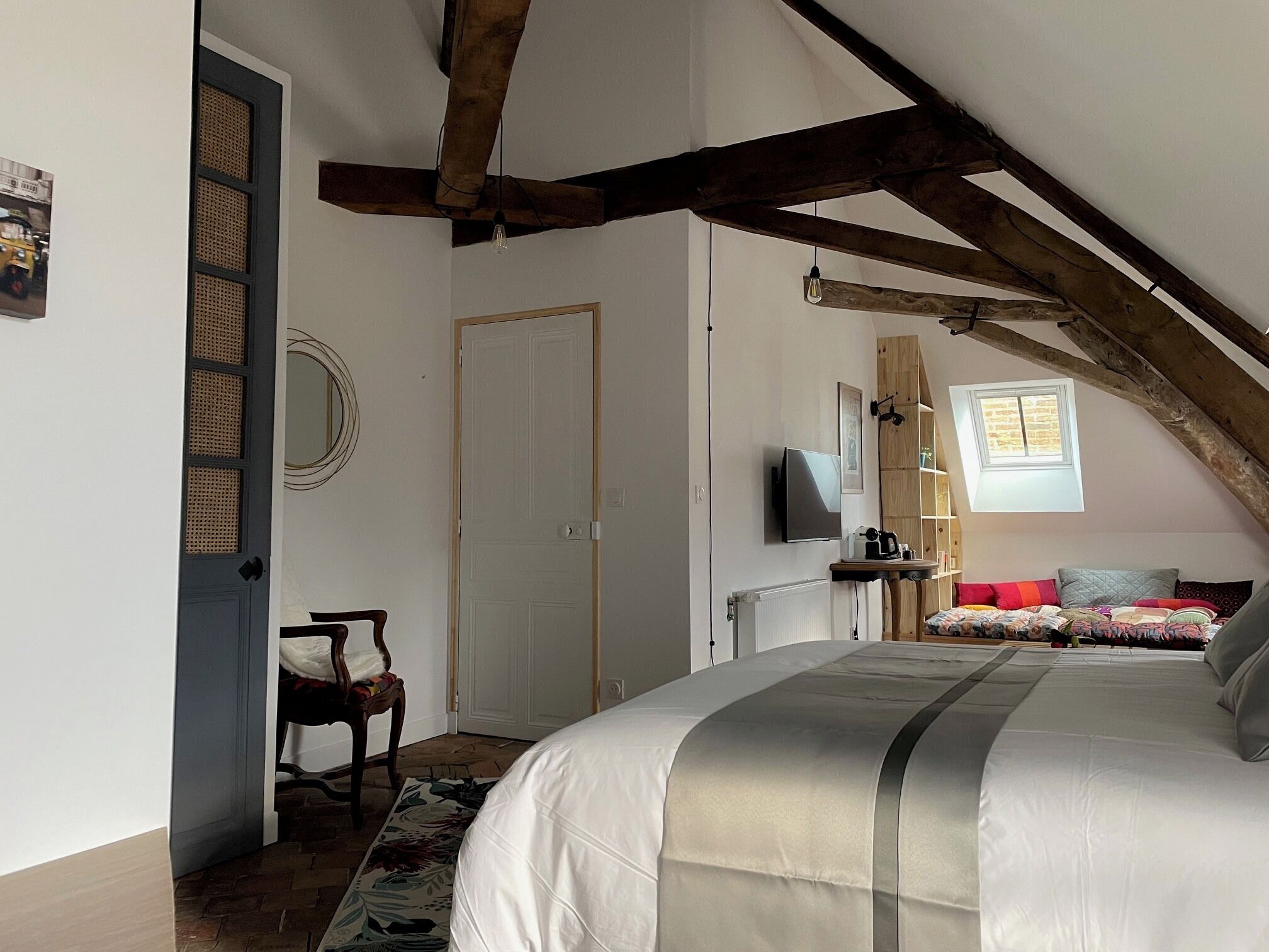 Un dormitorio con cama, una silla, un televisor, una ventana y una puerta.