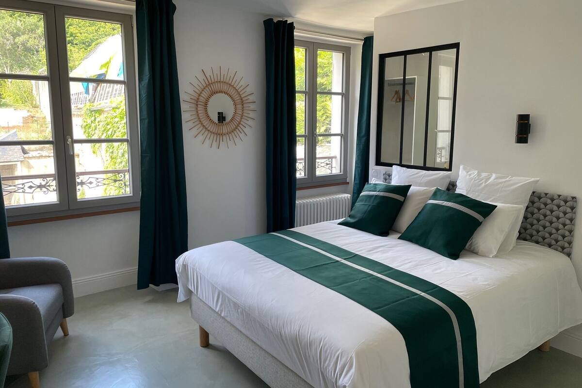 Une chambre avec un grand lit, un miroir et une vue sur l’extérieur par les fenêtres.