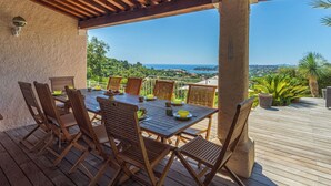 Une terrasse extérieure avec une table et des chaises en bois, une pergola au-dessus et une vue panoramique sur la mer et les collines.