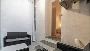 A small outdoor seating area with wicker furniture, a tiled floor, and a white wall.