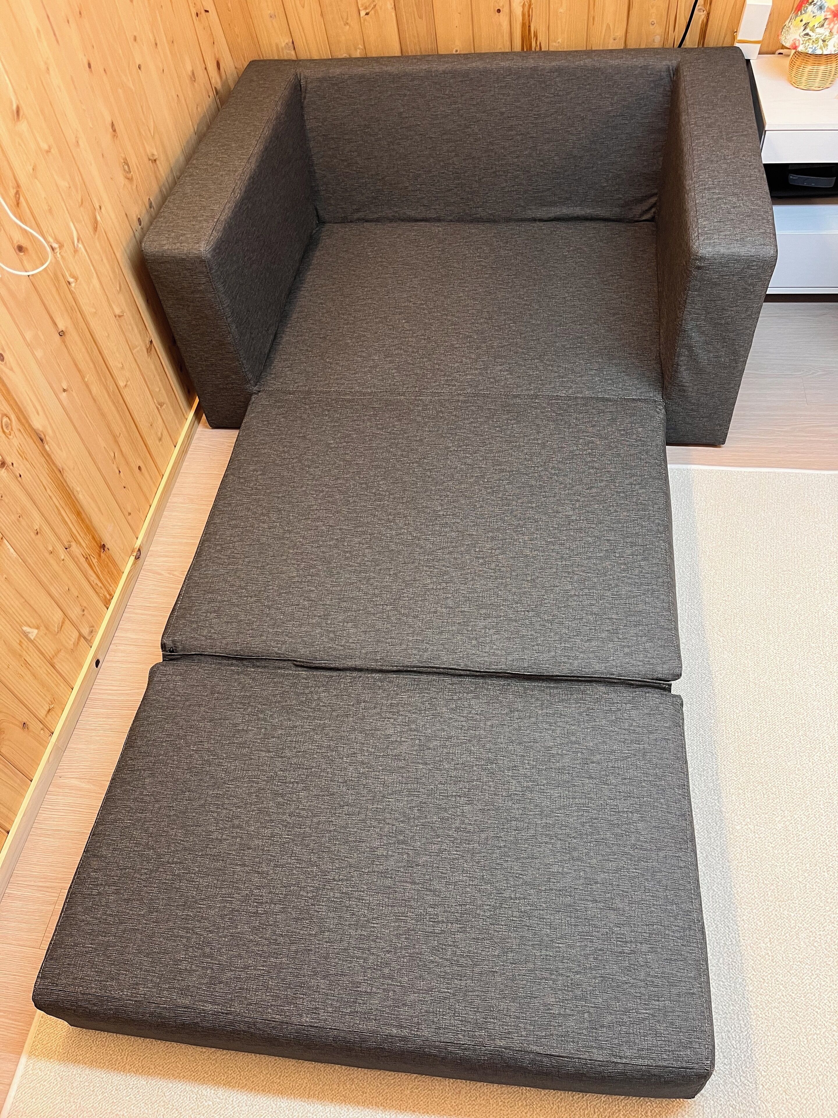 A sofa with a grey fabric and wooden paneling on the walls.