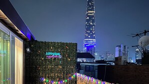 Un área de estar al aire libre con una mesa y sillas, un muro decorativo con luces y vistas a un edificio alto al fondo.