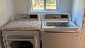A laundry room with two stacked washer and dryer units, a window above, and a door to the right.