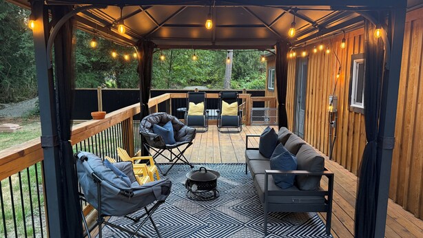 A covered outdoor deck with a wooden floor, a black and white patterned rug, a sofa, a chair, and string lights.
