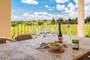 A table set with wine glasses, a bottle, and a candle on a balcony with a vineyard view.