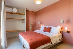 Ein Schlafzimmer mit einem Bett, einer Ablage mit gerollten Handtüchern, einer Pendelleuchte und einer Vase mit getrockneten Pflanzen.