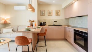 A modern kitchen with a central island, bar stools, a built-in oven, and a dining area with a sofa and lamp. - Domus Olivea (Estézargues)