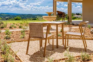 An outdoor seating area with a table and chairs, a decorative stone basin, and a view of the countryside.