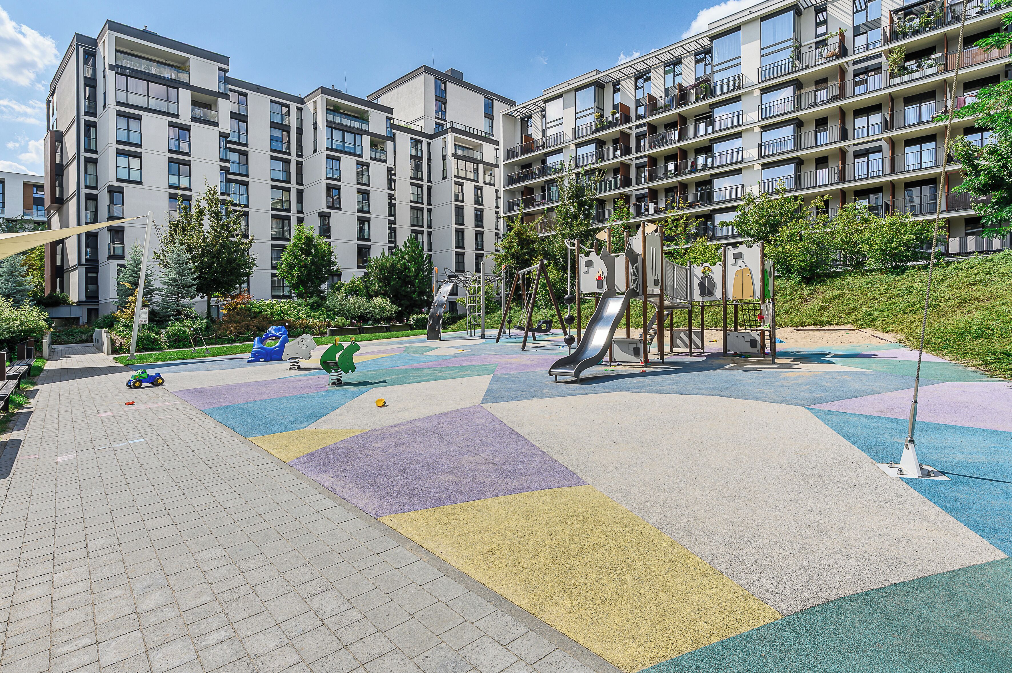 Een speeltuin met een glijbaan en klimconstructies, omringd door een verhard gebied met kleurrijke tegels.