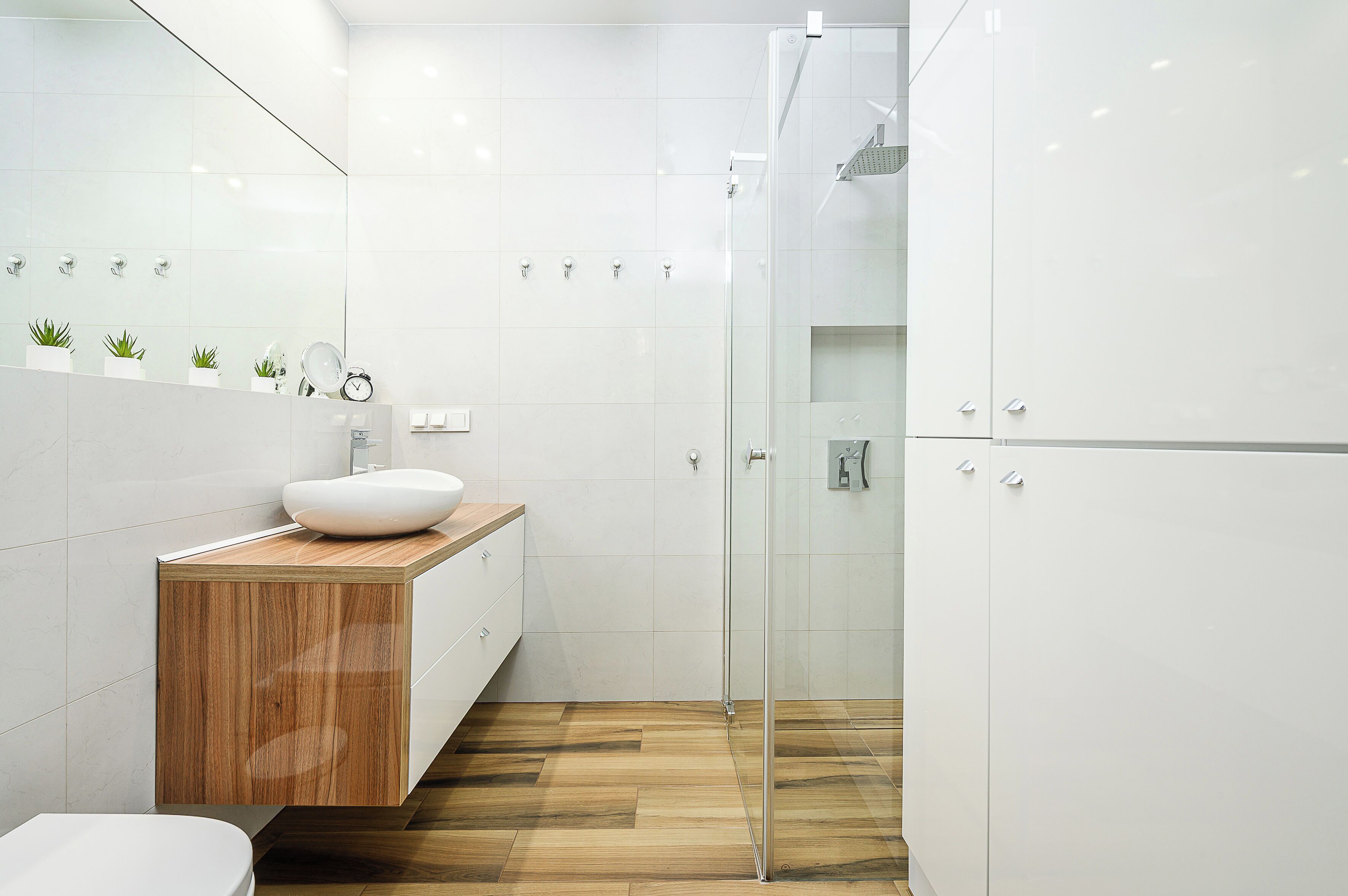 A modern bathroom with a wooden vanity, a white sink, and a glass shower enclosure.