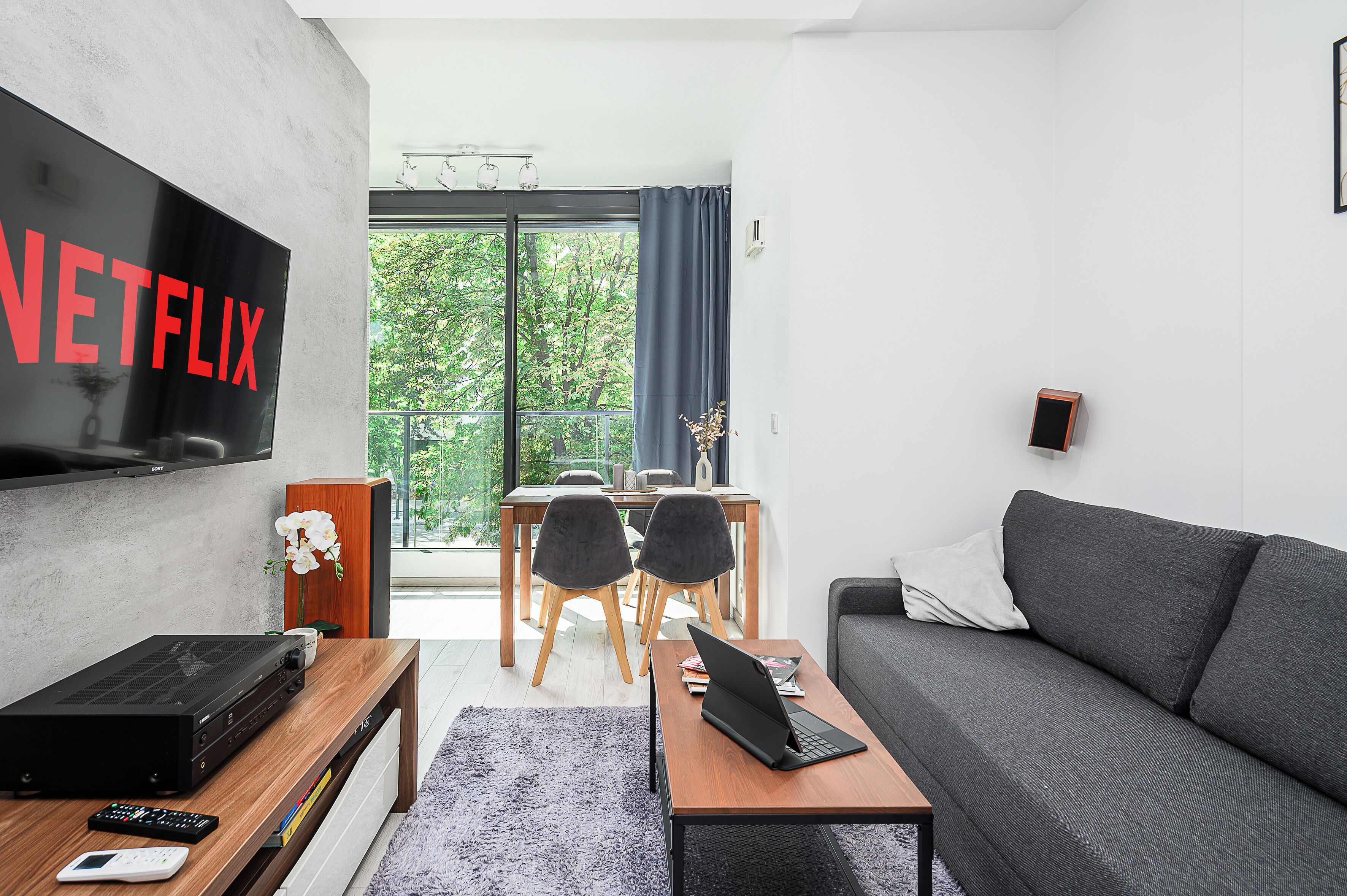 Een moderne woonkamer met een flatscreen televisie, een laptop, een bank en een eethoek met stoelen en een tafel.