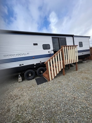 A large RV with a ramp leading to a door, parked on gravel.