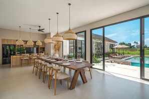 A modern kitchen with a dining area, large windows, and a pool view. - Villa Anarya Ubud (Ubud)