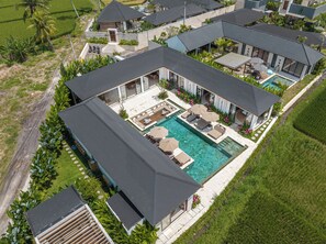 A modern resort with a large swimming pool, multiple outdoor seating areas, and lush landscaping. - Villa Anarya Ubud (Ubud)