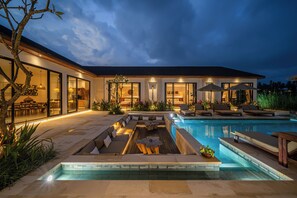 Une maison moderne dotée d’une piscine, d’un espace salon extérieur et d’un patio bien éclairé.