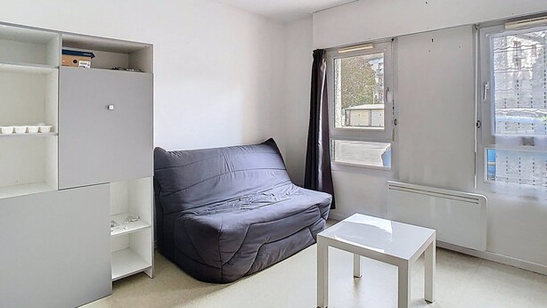 A compact room with a grey sofa, a small white table, and built-in shelving. - Le Wellington, Arras (Arras)
