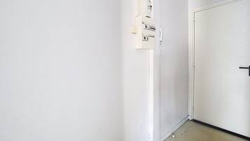 Un corridoio stretto con una porta bianca a destra e prese elettriche sulla parete sinistra.