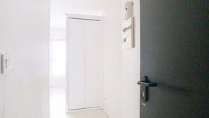 A narrow hallway with a white door at the end, a dark door on the right, and a light switch on the left. - Le Wellington, Arras (Arras)