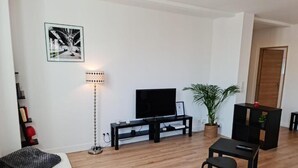 A modern living room with a flat-screen TV, a black sofa, a small table, and a potted plant. - The Scottman House (Arras)
