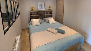Une chambre à coucher moderne avec un cadre de lit en bois, une tête de lit intégrée et une grande fenêtre équipée de stores.