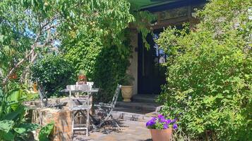 A stone pathway leading to a house with a green roof, surrounded by lush greenery and potted flowers.