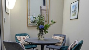Un coin repas avec une table ronde et quatre chaises, un vase de fleurs, un miroir et un tableau encadré au mur.