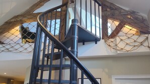 Un escalier en colimaçon avec une rampe en métal noir, des poutres en bois et un plafond à la structure en forme de réseau.